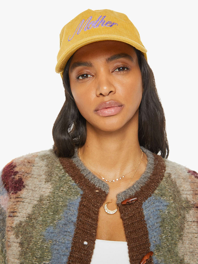 Front view of a model in a vintage-inspired trucker hat designed in mustard-yellow corduroy with MOTHER's name in lavender on the front.