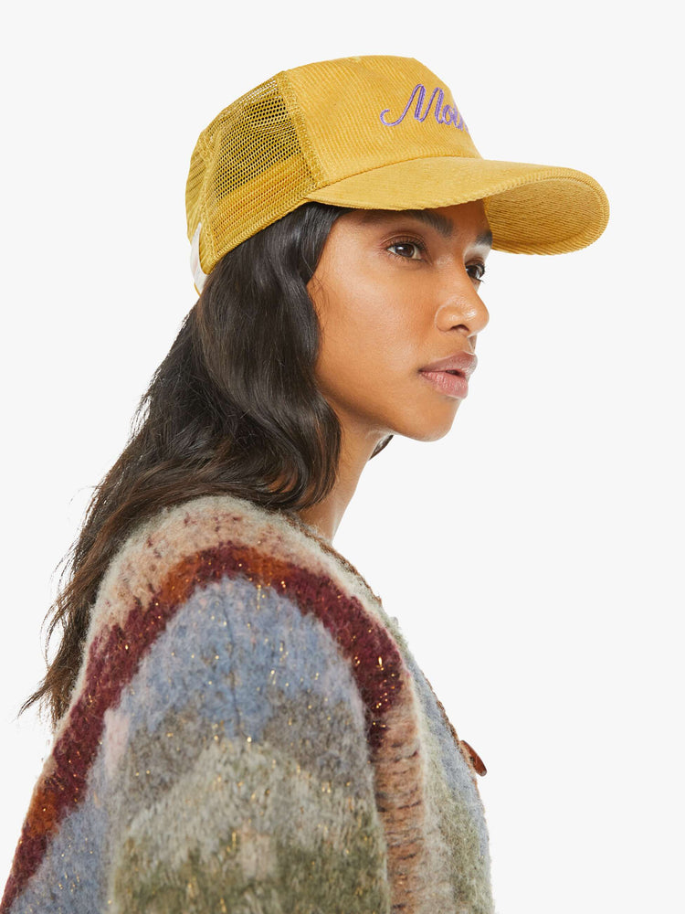 Side view of a model in a vintage-inspired trucker hat designed in mustard-yellow corduroy with MOTHER's name in lavender on the front.