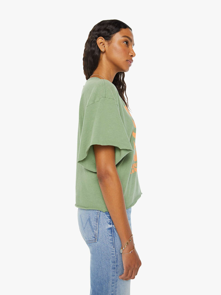 Side view of a woman in a sage green  oversized crewneck tee with drop shoulders and raw hems with a peach bird graphic with text on the front.