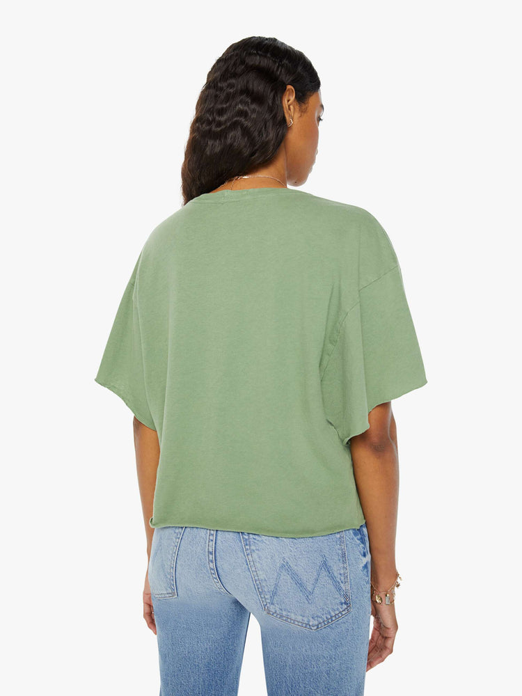 Back view of a woman in a sage green  oversized crewneck tee with drop shoulders and raw hems with a peach bird graphic with text on the front.