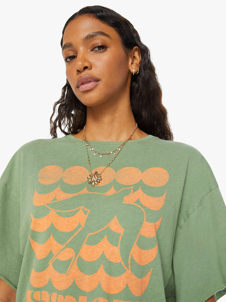 Detailed view of a woman in a sage green  oversized crewneck tee with drop shoulders and raw hems with a peach bird graphic with text on the front.