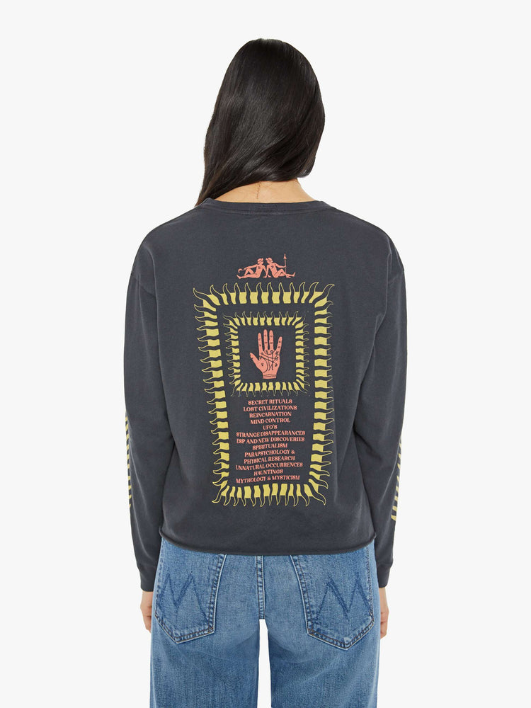 Side view of a woman in an oversized long-sleeve crewneck with a slightly cropped cutoff hem in faded black with mystical graphics.