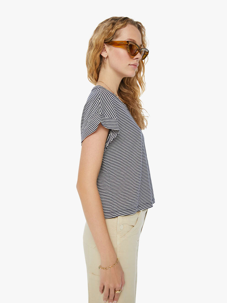 Side view of a woman in a nautical white and navy striped cropped crewneck tee with short rolled sleeves, a chest pocket and a boxy fit. 