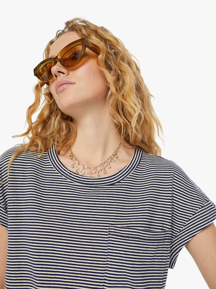 Detailed view of a woman in a nautical white and navy striped cropped crewneck tee with short rolled sleeves, a chest pocket and a boxy fit. 