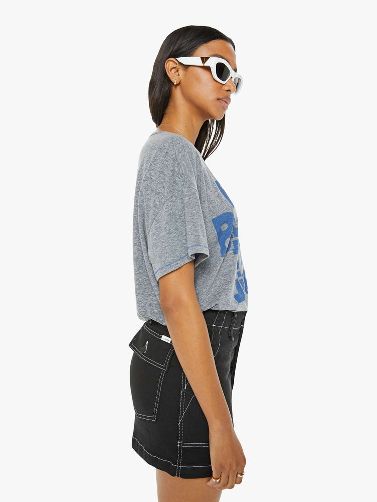 Side view of a woman in a heathered grey oversized tee with drop shoulders and loose boxy fit with blue text graphic.