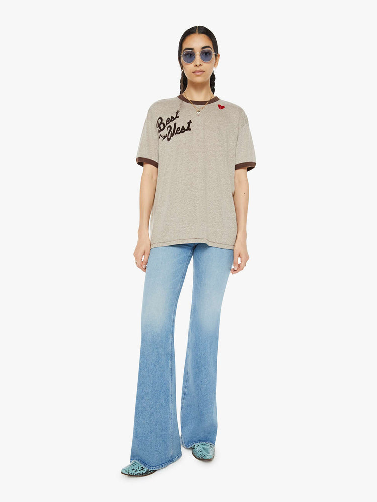 Full body view of a woman marled tan oversized tee with drop shoulders and a loose fit with a red heart near the collar.