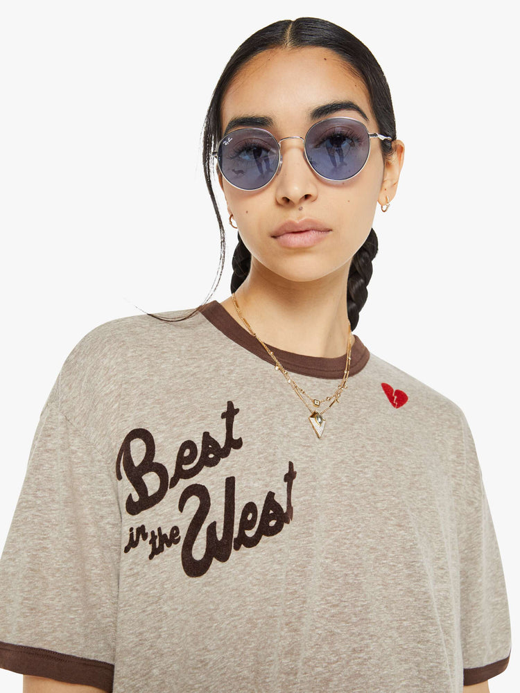 Close up view of a woman marled tan oversized tee with drop shoulders and a loose fit with a red heart near the collar.