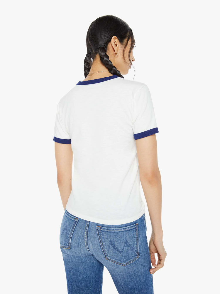 Back view of a woman in a white tee features a text graphic in yellow, blue and red on the front and navy trim on the neck and sleeves.