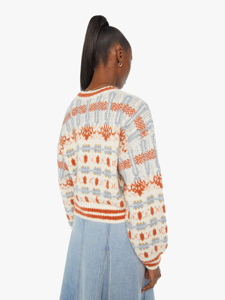 Back view of a woman in a sweater with dramatic drop shoulders, extra-long sleeves, a slightly cropped hem and a boxy fit in cream, orange and baby blue.