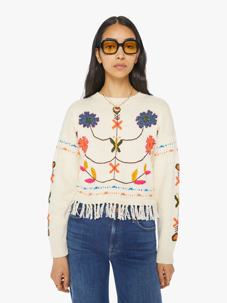 Front view of a woman in an off-white cropped crewneck sweater with hand-embroidered flowers, drop shoulders and a cropped, fringed hem.