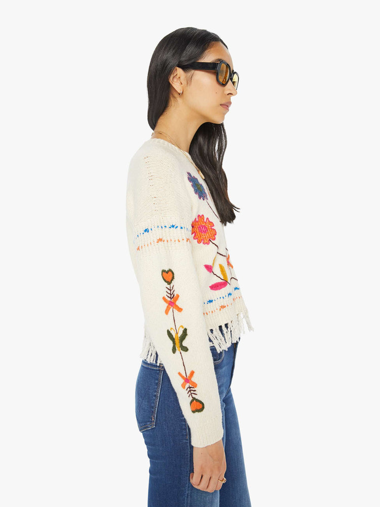 Side view of a woman in an off-white cropped crewneck sweater with hand-embroidered flowers, drop shoulders and a cropped, fringed hem.