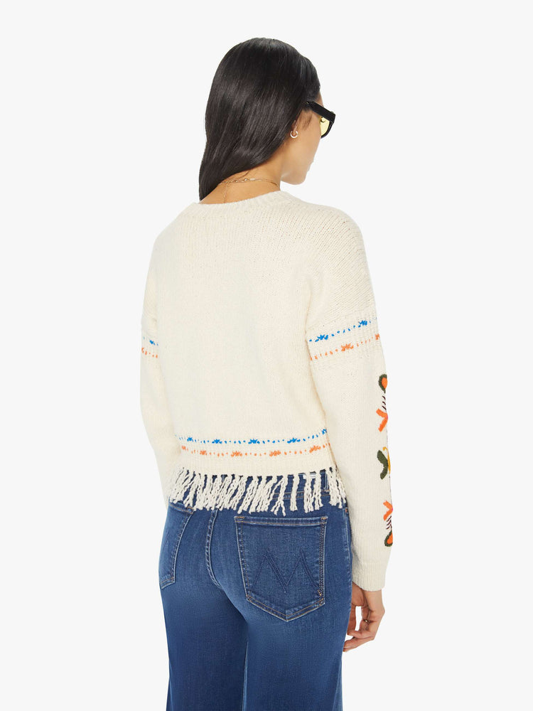 Back view of a woman in an off-white cropped crewneck sweater with hand-embroidered flowers, drop shoulders and a cropped, fringed hem.