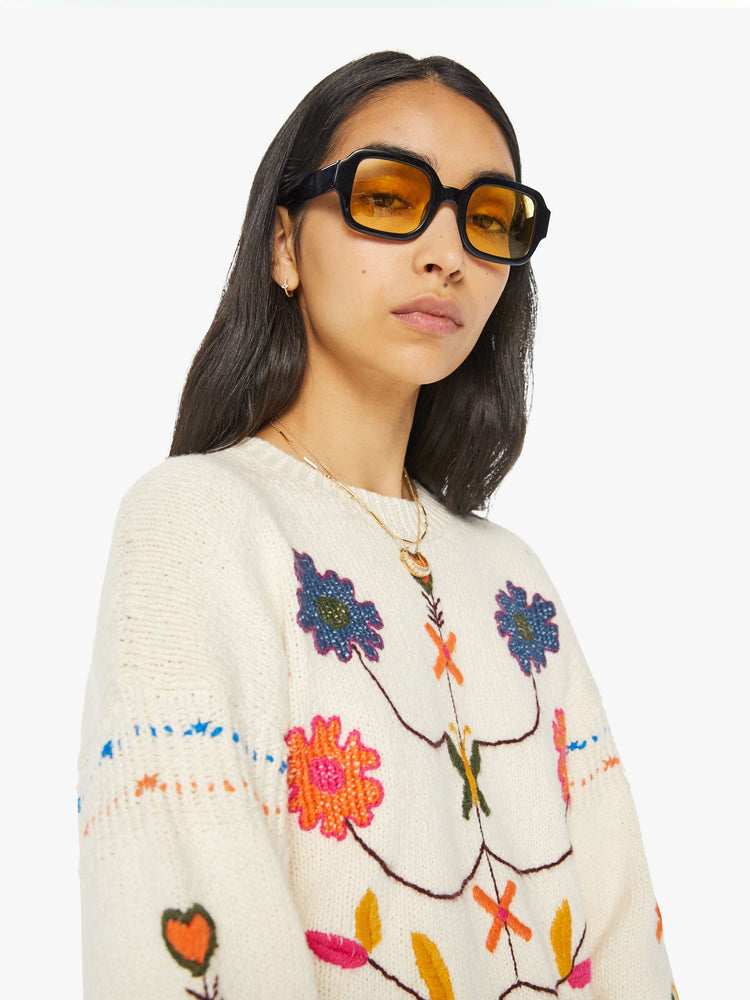 Detailed view of a woman in an off-white cropped crewneck sweater with hand-embroidered flowers, drop shoulders and a cropped, fringed hem.