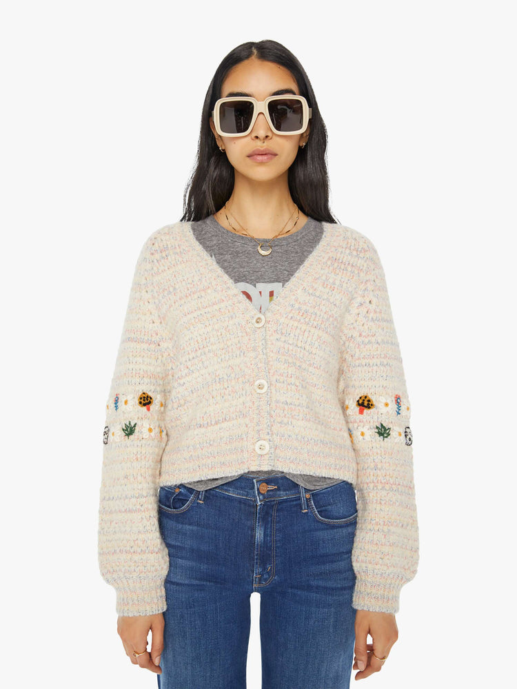 Front view of a woman in an off-white V-neck cardigan with colorful speckles throughout and embroidered details at the elbows.