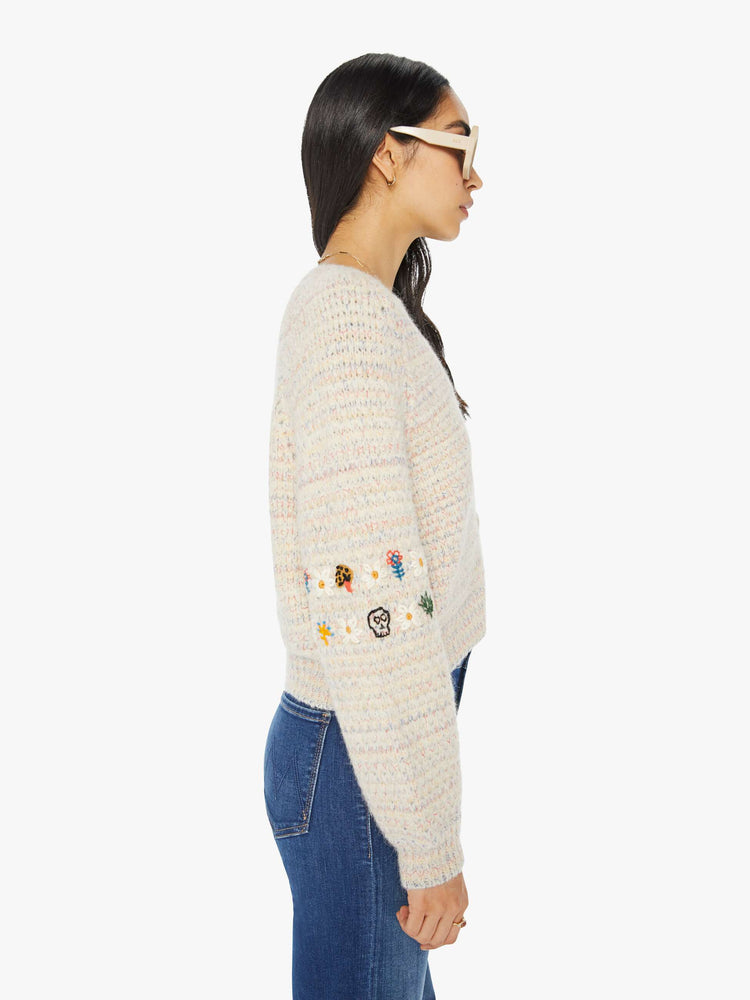 Side view of a woman in an off-white V-neck cardigan with colorful speckles throughout and embroidered details at the elbows.