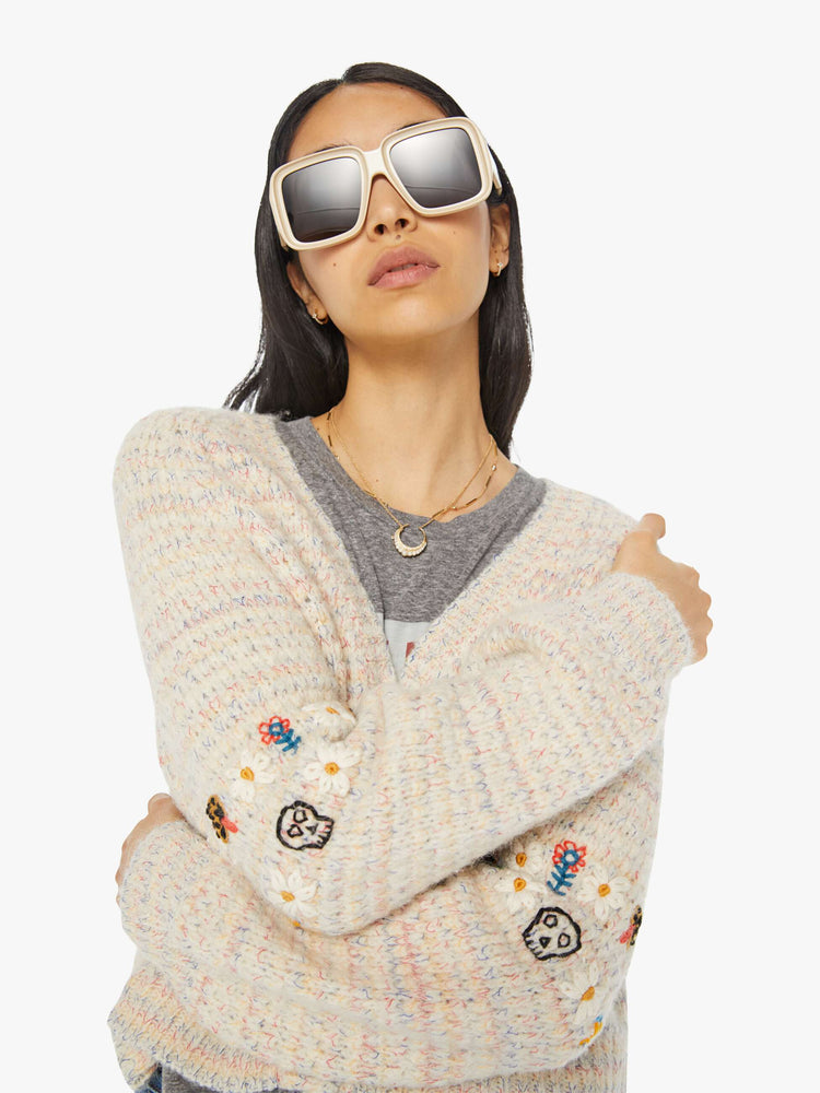 Detailed view of a woman in an off-white V-neck cardigan with colorful speckles throughout and embroidered details at the elbows.