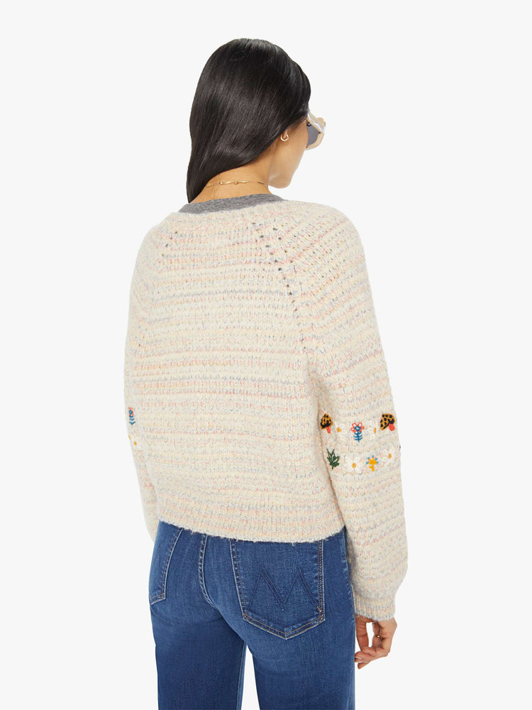 Back view of a woman in an off-white V-neck cardigan with colorful speckles throughout and embroidered details at the elbows.