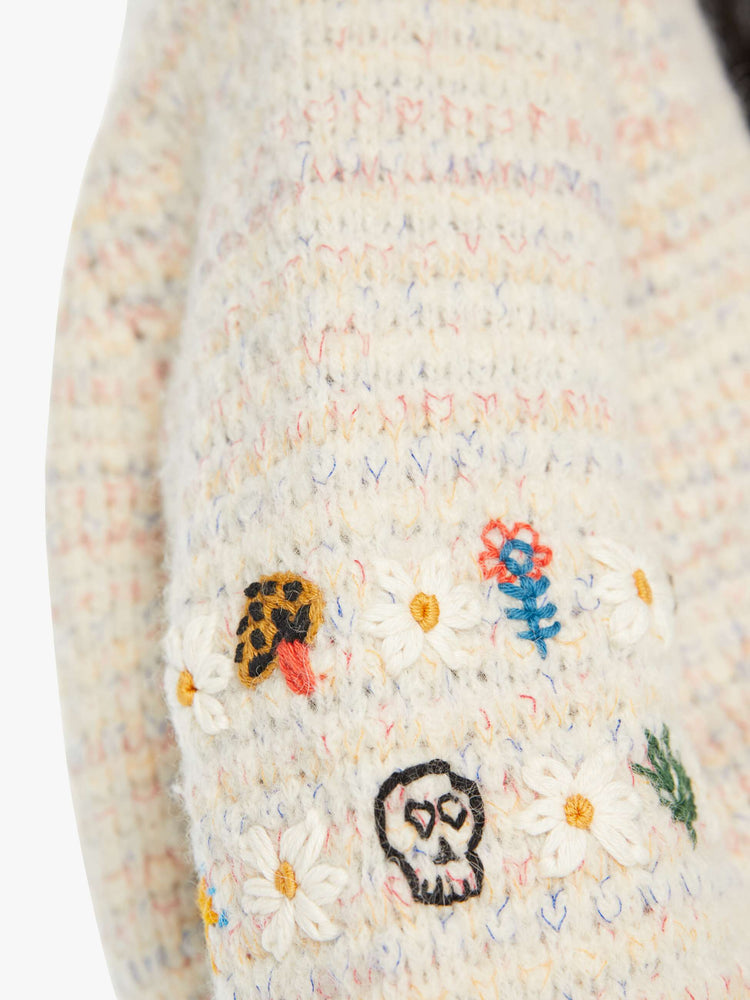 Swatch view of a woman in an off-white V-neck cardigan with colorful speckles throughout and embroidered details at the elbows.