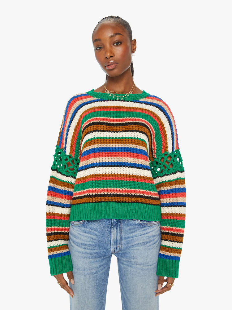 Front view of a woman in a slightly cropped crewneck sweater in a colorful horizontal stripe pattern with green crochet panels on the sleeves.