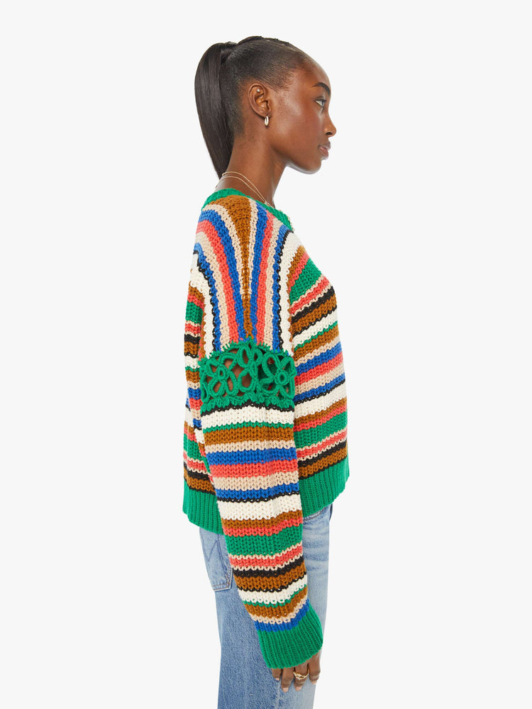 Side view of a woman in a slightly cropped crewneck sweater in a colorful horizontal stripe pattern with green crochet panels on the sleeves.