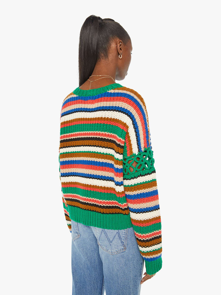 Back view of a woman in a slightly cropped crewneck sweater in a colorful horizontal stripe pattern with green crochet panels on the sleeves.