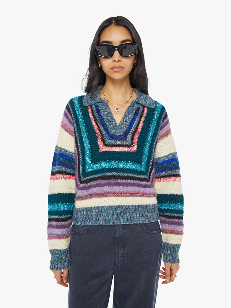 Front view of  woman in a geometric stripe pattern in cool-toned shades of lavender, cream, black and navy V-neck sweater with slightly dropped shoulders, ribbed hems and a boxy fit. 