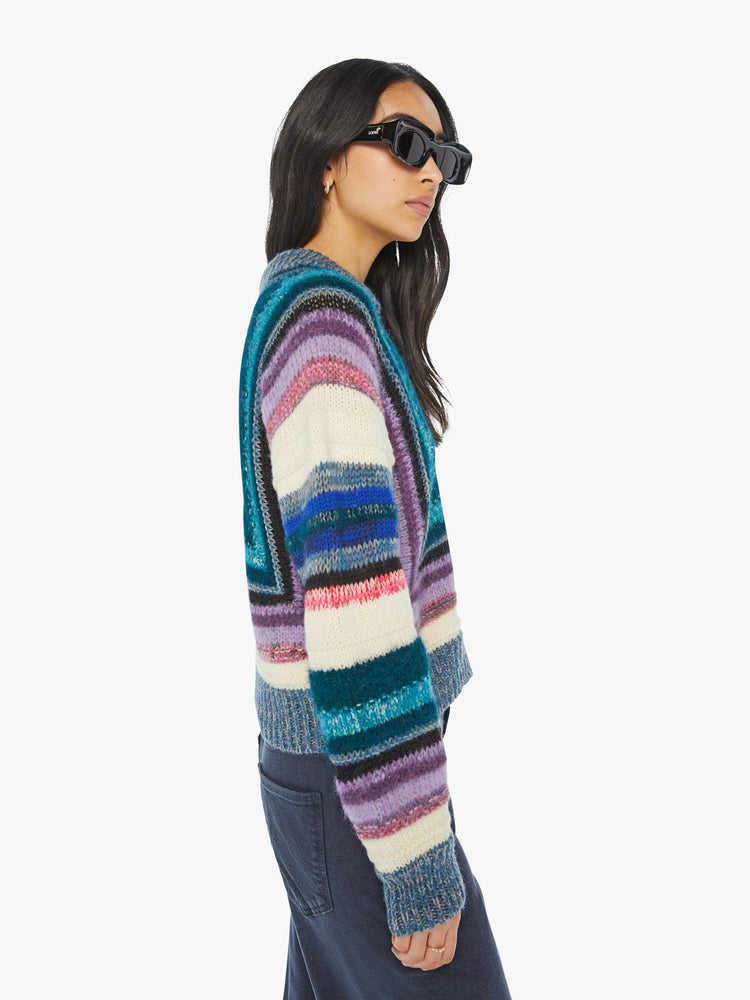 Side view of woman in a geometric stripe pattern in cool-toned shades of lavender, cream, black and navy collared V-neck sweater with slightly dropped shoulders, ribbed hems and a boxy fit.