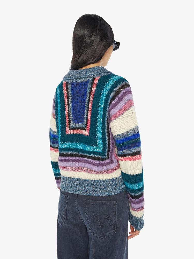 Back view of woman in a geometric stripe pattern in cool-toned shades of lavender, cream, black and navy collared V-neck sweater with slightly dropped shoulders, ribbed hems and a boxy fit.