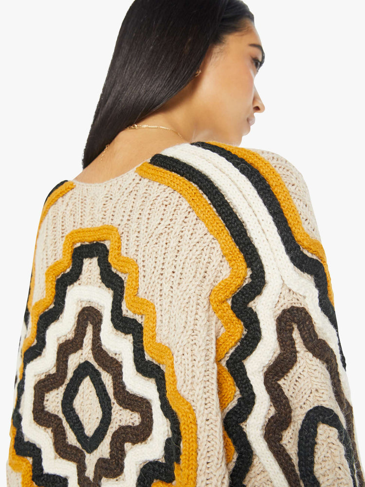 Close up view of a woman in knit top with a deep V-neck, single-button closure, drop shoulders and a cropped fit in a beige color and fringe sleeves. 