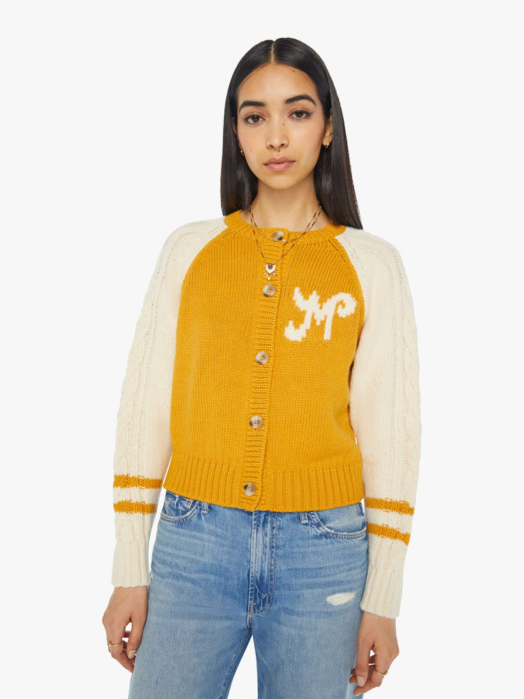 Front view of a woman letterman-inspired crewneck cardigan with raglan sleeves, ribbed hems and a slightly cropped fit in a mustard yellow with cream sleeves.