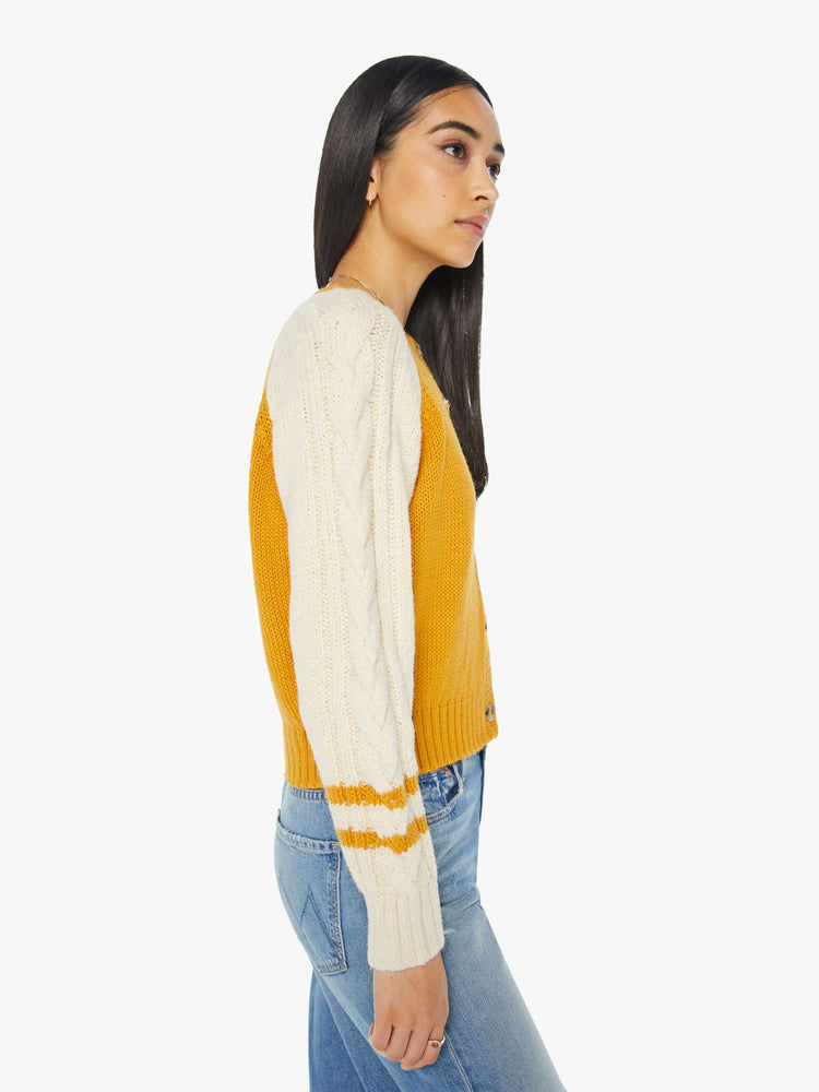 Side view of a woman letterman-inspired crewneck cardigan with raglan sleeves, ribbed hems and a slightly cropped fit in a mustard yellow with cream sleeves.