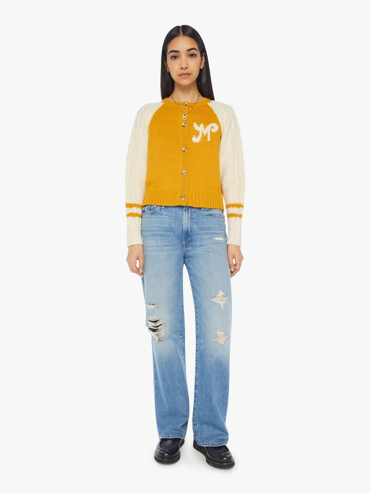 Full body view of a woman letterman-inspired crewneck cardigan with raglan sleeves, ribbed hems and a slightly cropped fit in a mustard yellow with cream sleeves.