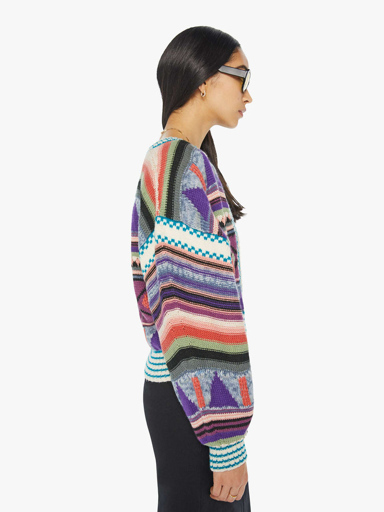 Side view of a woman in a crewneck cardigan with drop shoulders, ribbed hems and a cropped fit in a cool-toned pattern with geometric shapes and white and teal stripes at the hems