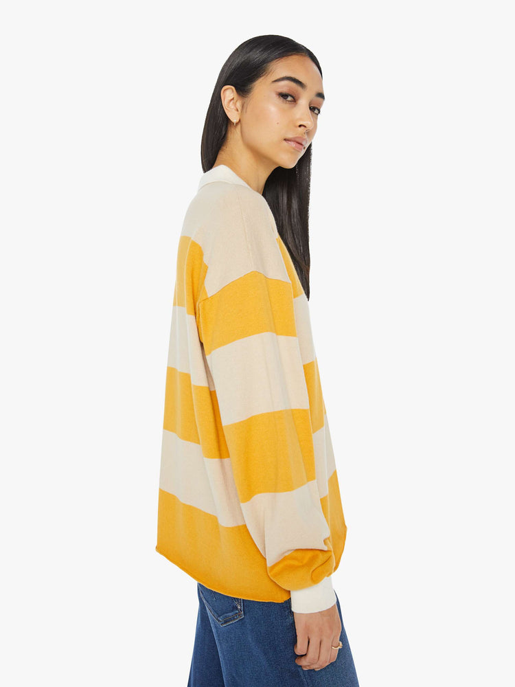 Side view of a woman polo  with drop shoulders, extra-long sleeves, a loose, oversized fit and a raw hem in a cream and yellow horizontal stripes.