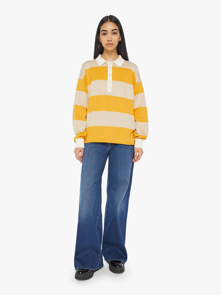 Full body view of a woman polo  with drop shoulders, extra-long sleeves, a loose, oversized fit and a raw hem in a cream and yellow horizontal stripes.