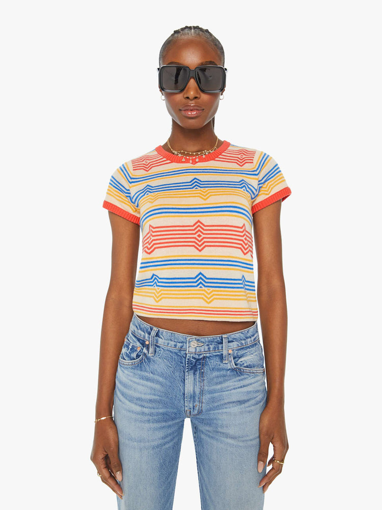 Front view of a woman in a light tan scoop neck baby tee with a horizontal stripe pattern in red, blue and yellow.