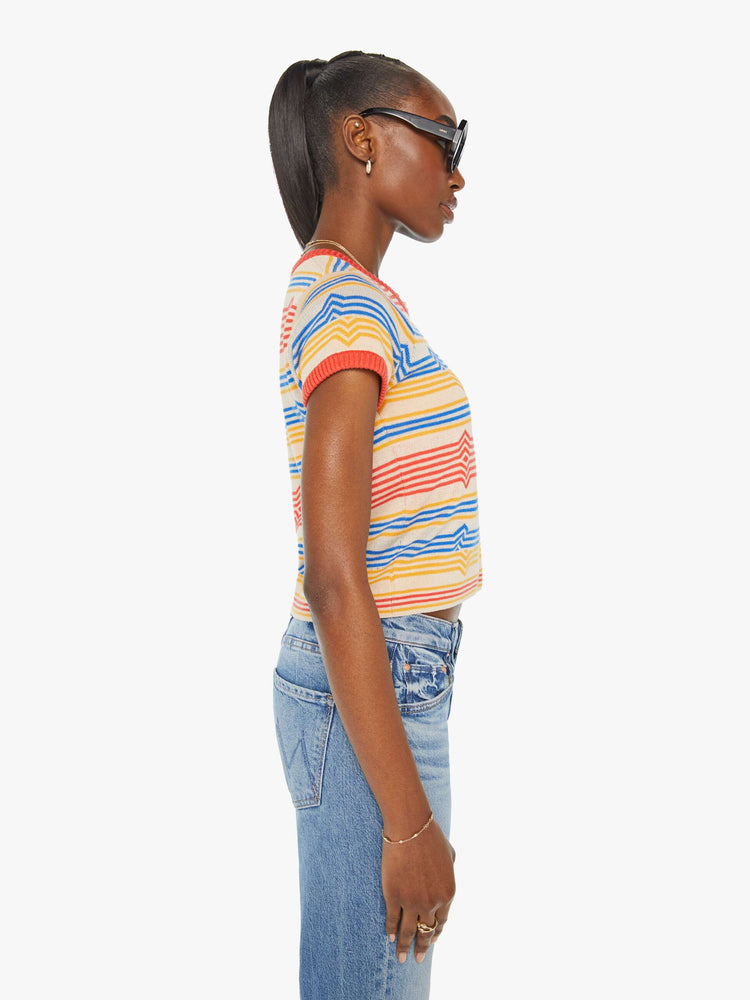 Side view of a woman in a light tan scoop neck baby tee with a horizontal stripe pattern in red, blue and yellow.