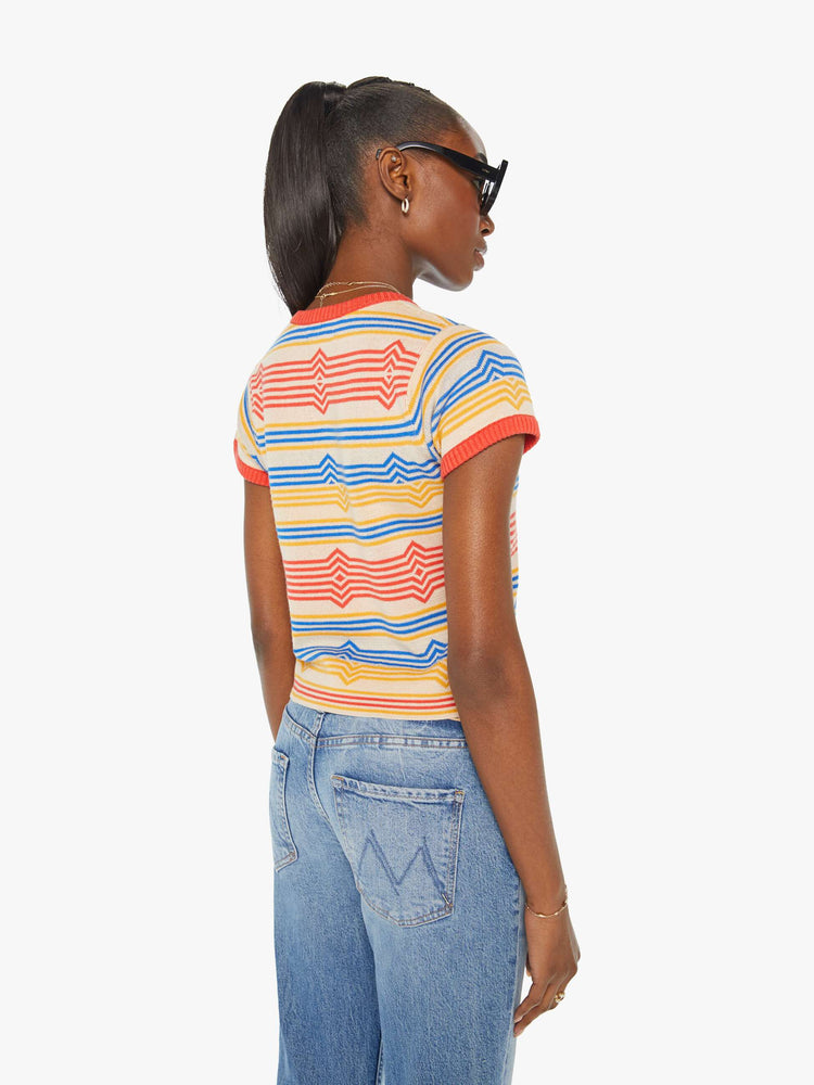 Back view of a woman in a light tan scoop neck baby tee with a horizontal stripe pattern in red, blue and yellow.