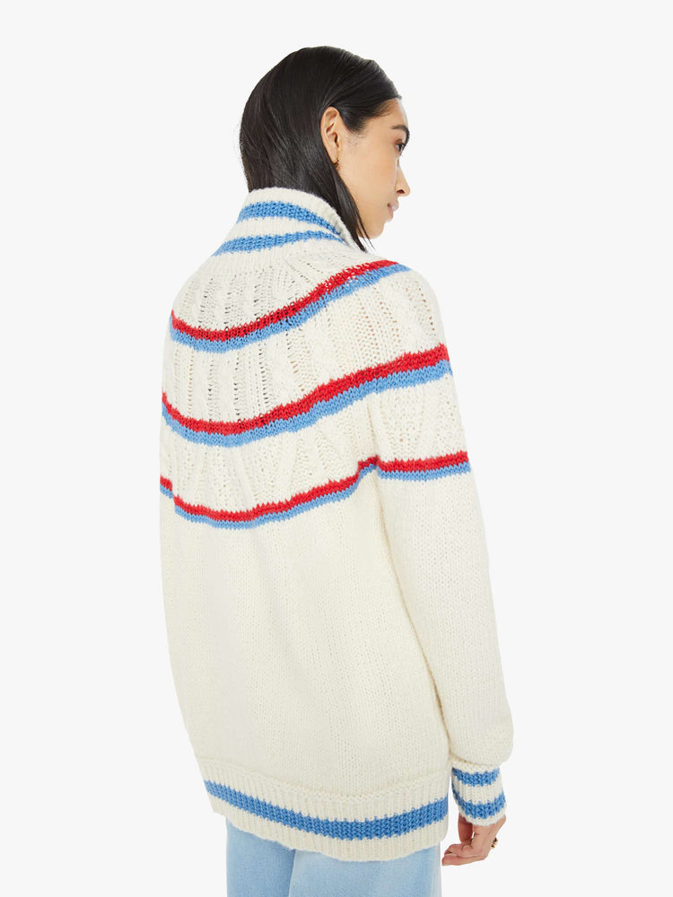 Back view of a woman in a mock neck cardigan sweater with drop shoulders, front patch pockets, ribbed hems, buttons down the front and a slouchy fit in a cream color with red and blue stripes.