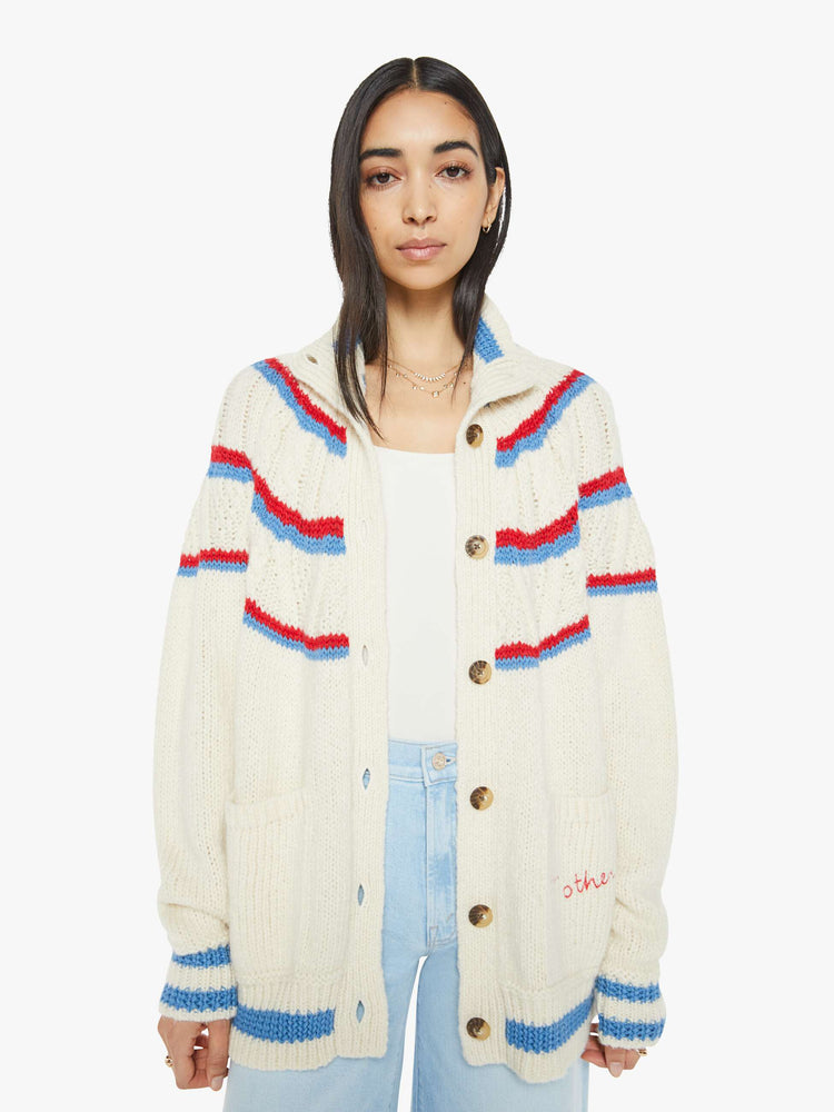 Front view of a woman in a mock neck cardigan sweater with drop shoulders, front patch pockets, ribbed hems, buttons down the front and a slouchy fit in a cream color with red and blue stripes.