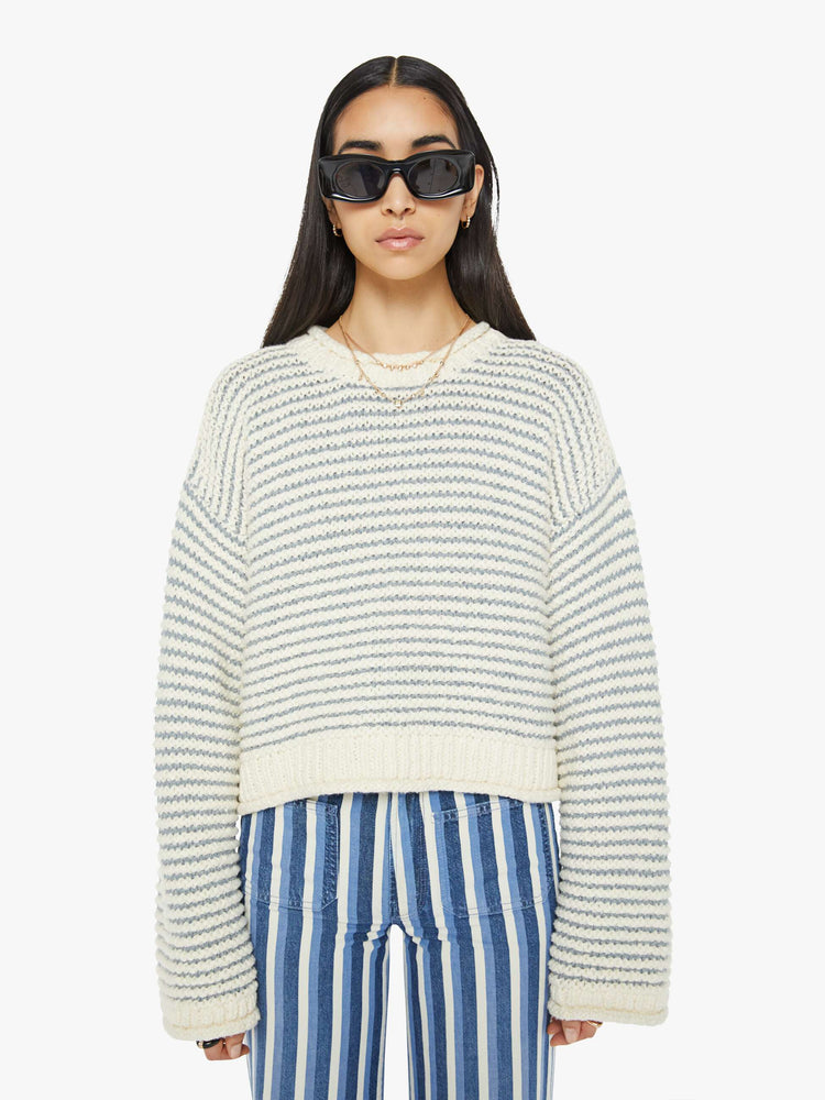 Front view of woman crewneck sweater with drop shoulders, long bell sleeves, rolled hems and a slightly cropped fit in off-white with baby blue horizontal stripes.