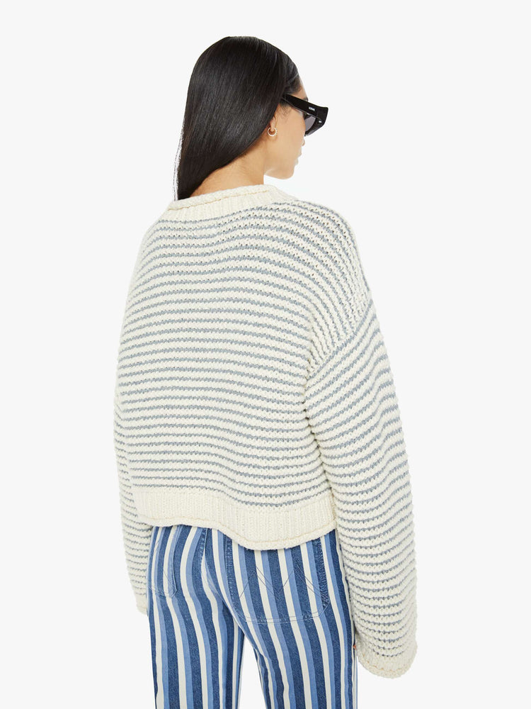 Back view of woman crewneck sweater with drop shoulders, long bell sleeves, rolled hems and a slightly cropped fit in off-white with baby blue horizontal stripes.