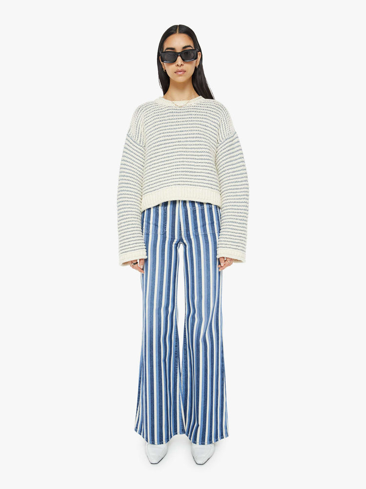 Full body view of woman crewneck sweater with drop shoulders, long bell sleeves, rolled hems and a slightly cropped fit in off-white with baby blue horizontal stripes.