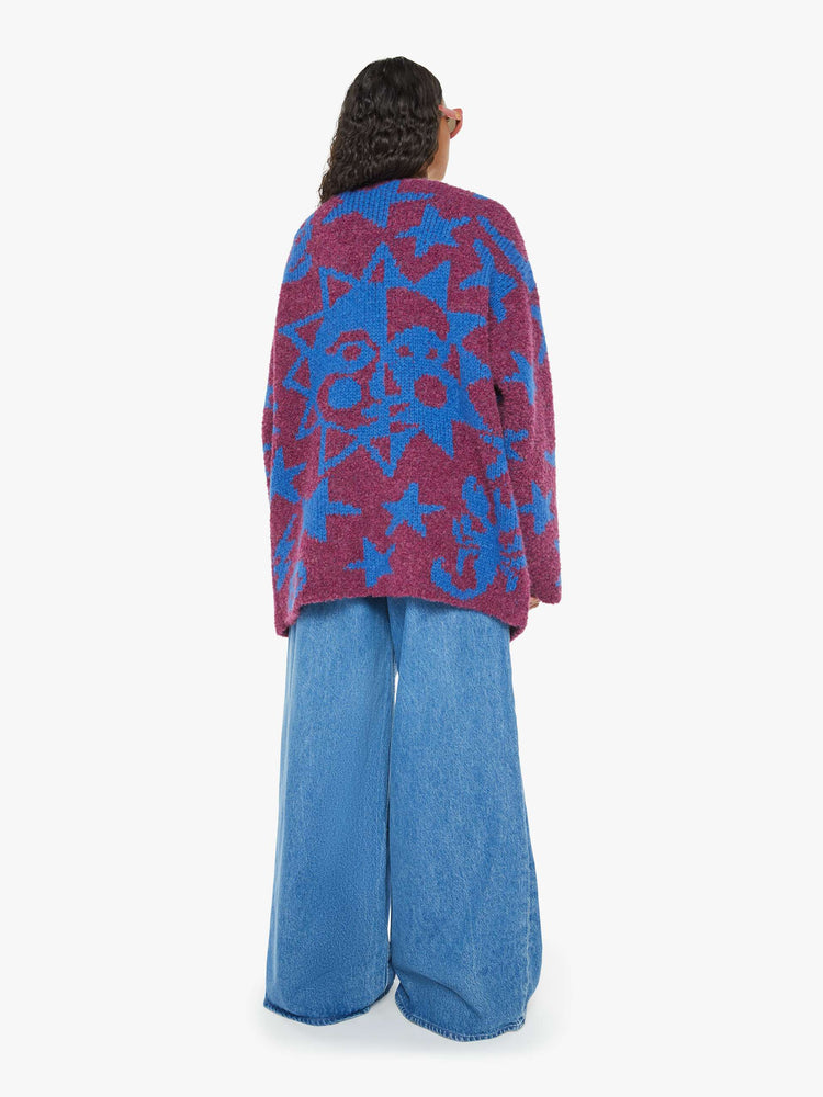 Back  view of a woman in an oversized v-neck cardigan with extra long sleeves in a maroon boucle with blue stars, moon and skulls.