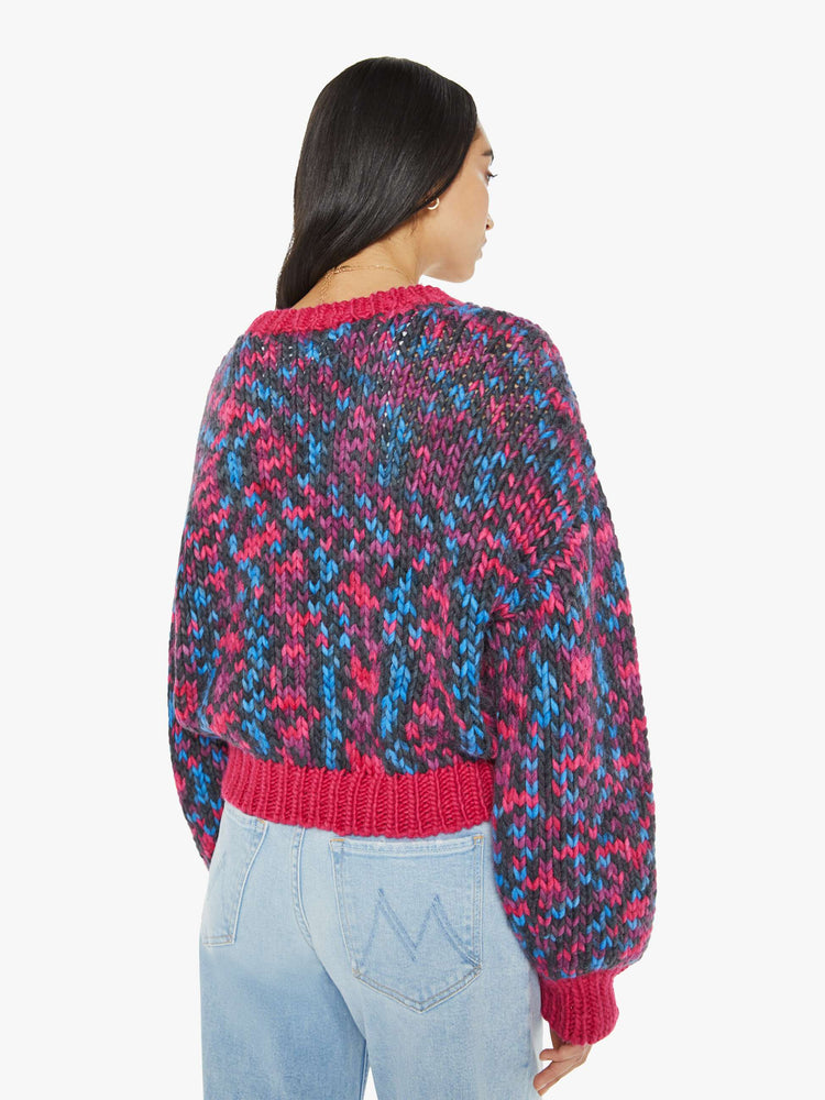 Back view of a woman in a crewneck sweater with drop shoulders, long bell sleeves, ribbed hems and a slightly cropped fit in shades of black, blue, pink and purple with hot pink trim.