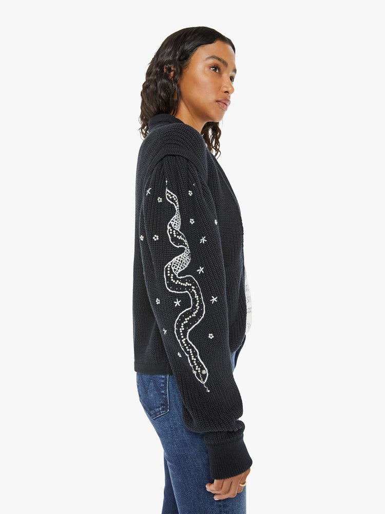 Left side view of a woman V-neck cardigan with a subtle shawl collar, drop shoulders, extra-long puffed sleeves and ribbed hems in black with embroidery snakes of sleeve.