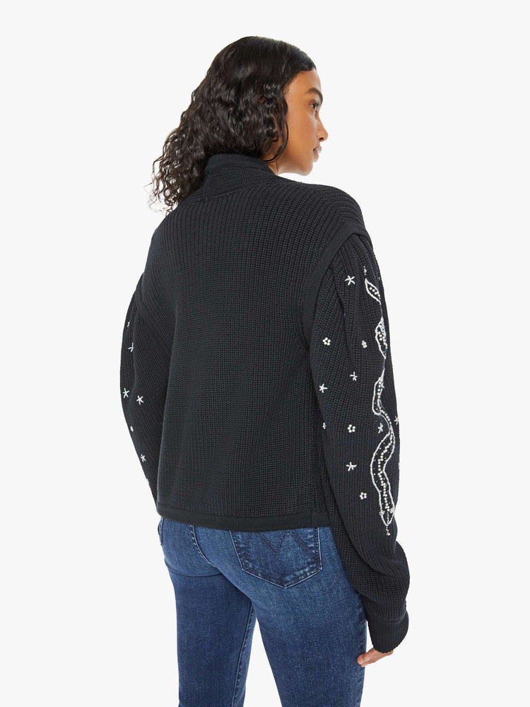 Back view of a woman V-neck cardigan with a subtle shawl collar, drop shoulders, extra-long puffed sleeves and ribbed hems in black with embroidery snakes of sleeve.