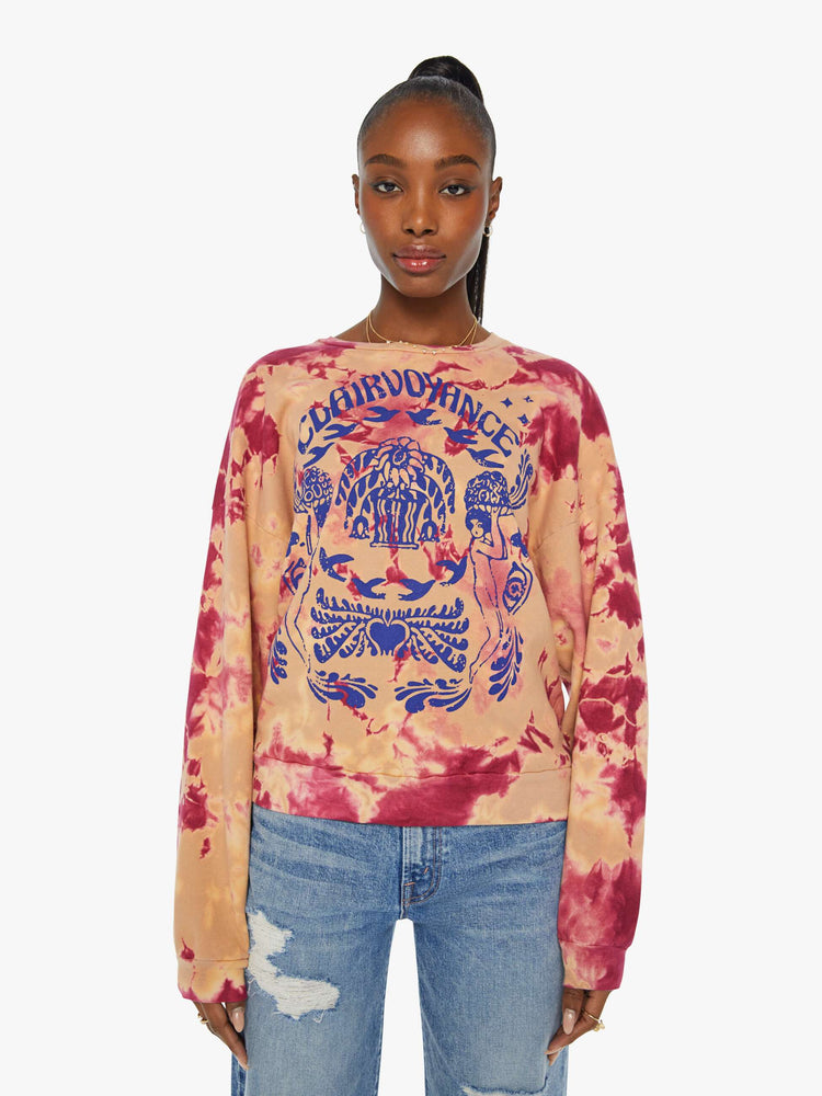 Front view of a woman in a hand-dyed in peach and raspberry-red tie dye sweatshirt with a trippy text graphic in blue on the front.