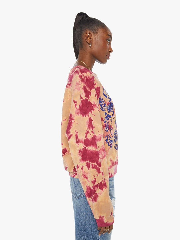 Side view of a woman in a hand-dyed in peach and raspberry-red tie dye sweatshirt with a trippy text graphic in blue on the front.