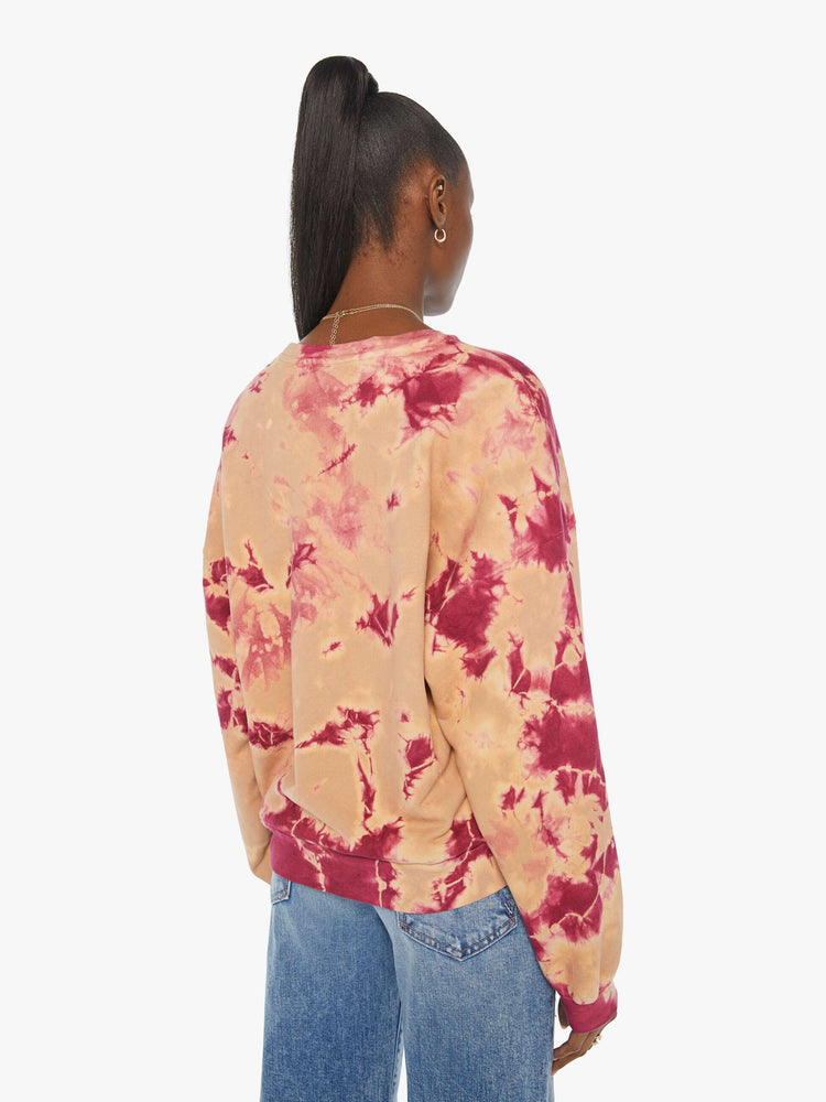 Back view of a woman in a hand-dyed in peach and raspberry-red tie dye sweatshirt with a trippy text graphic in blue on the front.